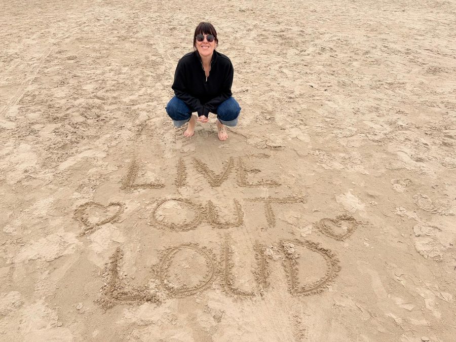A member at the beach with 'Live Out Loud' written in the sand